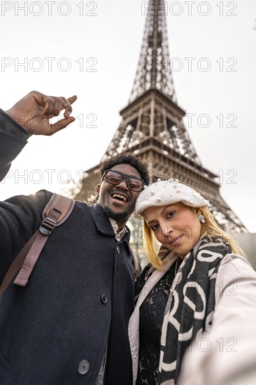 Diverse couple smiling for a selfie with the eiffel tower in the background, enjoying a romantic vacation in paris and capturing a joyful travel moment together