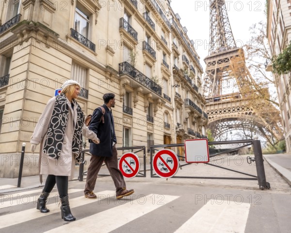 Diverse couple crossing a pedestrian street in paris, enjoying a city trip together with classical architecture and the iconic eiffel tower in the background