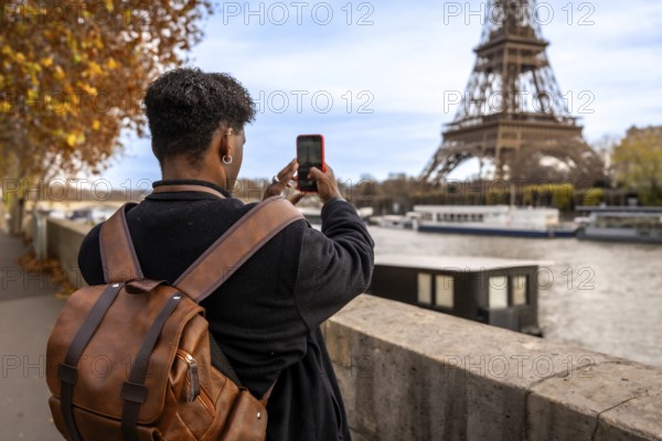 Tourist viewing and photographing the iconic eiffel tower from a bridge over the seine river in paris, experiencing travel and sightseeing in the famous european capital during autumn