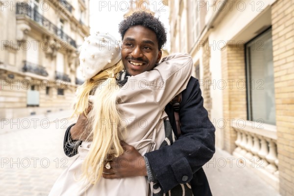 Loving diverse couple embracing and smiling on a charming parisian street, sharing a warm, romantic moment during an autumn stroll amid classic architecture and cozy fashion