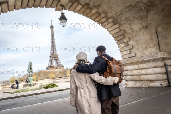 Couple embracing while walking under a stone arch bridge, enjoying a romantic travel sightseeing tour and admiring the iconic eiffel tower on a cloudy day in paris, france