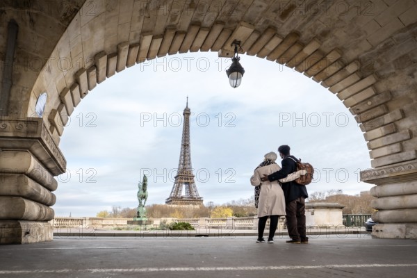 Couple stands embraced on pont de bir hakeim, framed by an ancient archway, observing the eiffel tower as a symbol of romance and travel, creating a lasting memory of their urban adventure