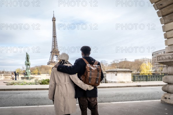 Adult black man and white woman embracing, looking at the iconic eiffel tower and cityscape of paris, enjoying travel and romance during a european vacation