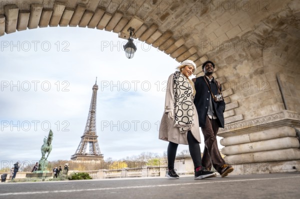 Young couple traveling through paris, france, walking under an archway with the iconic eiffel tower prominently featured in the background, enjoying a city trip together