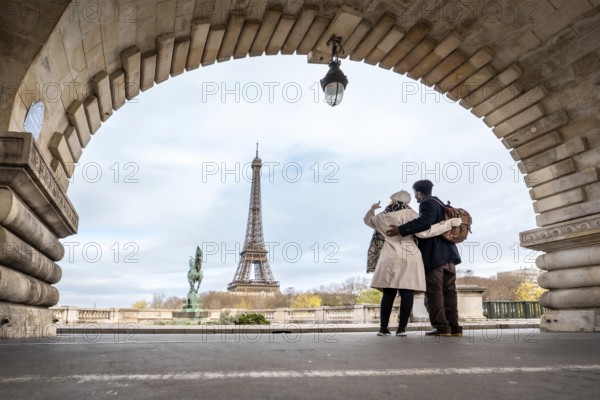Loving couple embraces under an arched bridge in paris, taking a selfie with the eiffel tower in the background while enjoying romance and sightseeing in the city