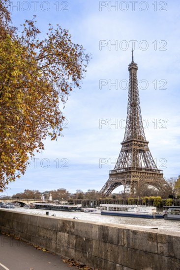 Iconic eiffel tower towering over the seine river in paris, with tour boats navigating the water and vibrant autumn leaves on trees reflecting seasonal travel and european tourism