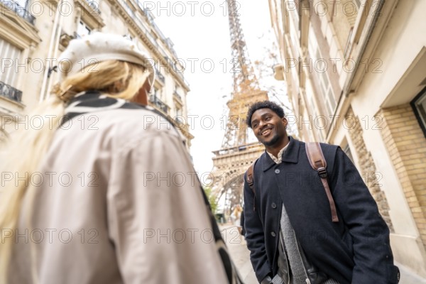 Happy young african american man smiling at his partner while enjoying a romantic trip in paris, with the eiffel tower and cityscape in the blurred background