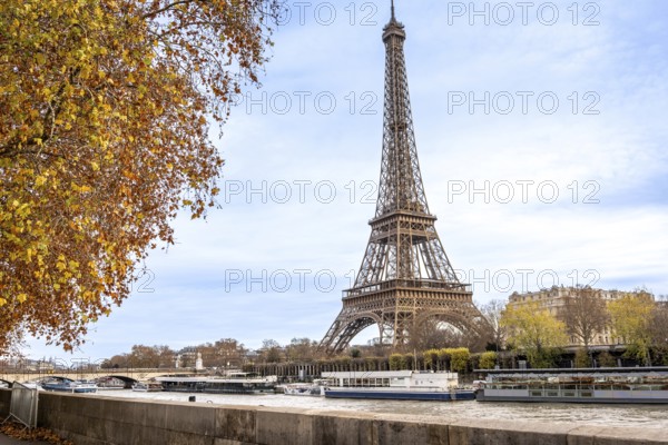 Eiffel tower rising beside the seine as tour boats glide past golden autumn trees and classic parisian buildings under a clear blue sky, reflecting on calm river waters