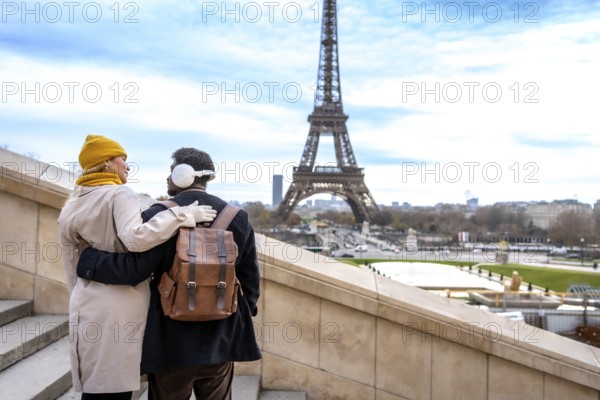 Young couple embracing on outdoor stairs with the eiffel tower in view, sharing a romantic winter moment in paris during a cozy sightseeing getaway