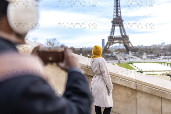 Tourist couple in paris enjoying the view as one photographs the eiffel tower and cityscape with a camera, capturing a romantic travel moment during their city tour