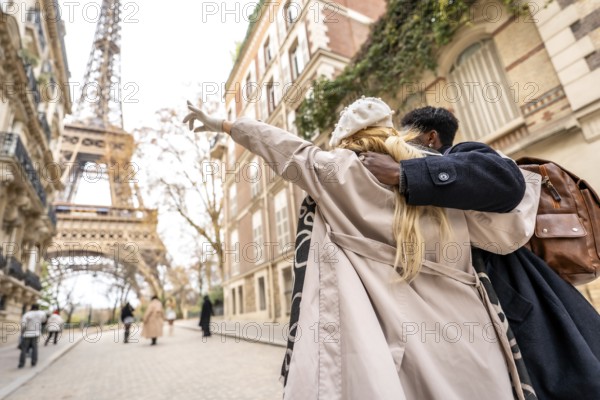 Young diverse couple embracing on a parisian street, with the woman pointing towards the distant eiffel tower, symbolizing travel, romance, and urban exploration