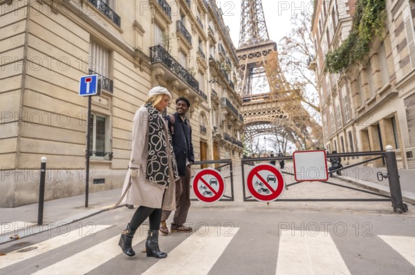 Diverse couple happily walking across a pedestrian crosswalk in a charming european street during autumn, enjoying a romantic trip with the eiffel tower in the background