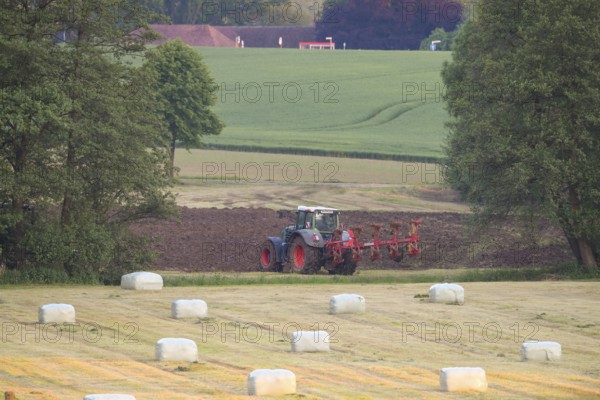 A tractor working in the field, surrounded by green fields and round bales of hay bales in a rural area, Osnabrücker Land, Lower Saxony, Germany