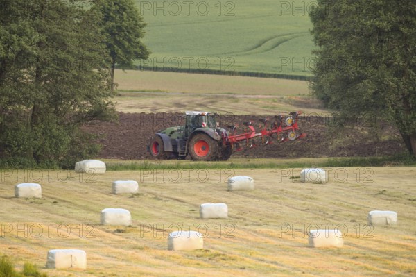A tractor plows a field surrounded by hay bales and trees in an agricultural scene, Osnabrücker Land, Lower Saxony, Germany