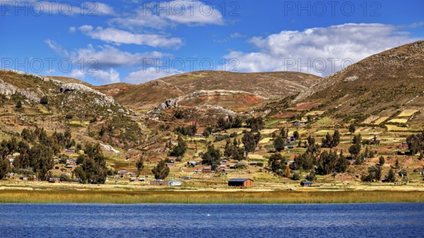Wide landscape with hills, a lake and small villages, under a blue sky full of clouds, The countryside and farmhouses on the island of Taquile in Lake Titicaca in Peru