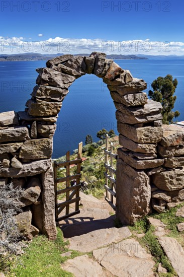 Stone archway with wooden gate in peaceful surroundings, with a view of vast blue lake and sky, stone gates on the island of Taquile in Lake Titicaca in Peru