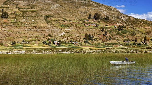 A boat on a reed lake surrounded by hills and a blue sky with clouds, the countryside and farmhouses on the island of Taquile in Lake Titicaca in Peru