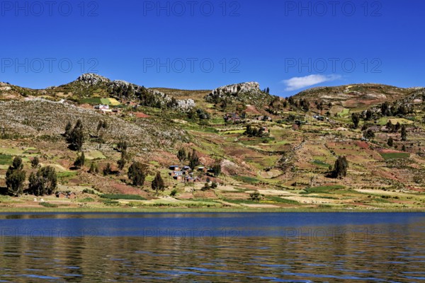 Wide fields stretch across rolling hills overlooking a lake, countryside and farmhouses on Taquile Island in Lake Titicaca in Peru