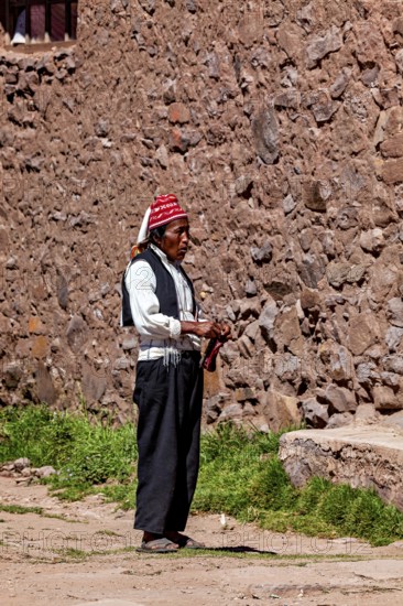 Elderly man wearing traditional clothes next to a stone wall under clear skies, The knitting men on Taquile Island in Lake Titicaca in Peru