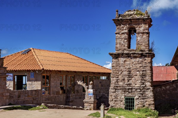 A historic stone building with a bell tower and red tile roofs against a blue sky, The historic church on Taquile Island in Lake Titicaca in Peru