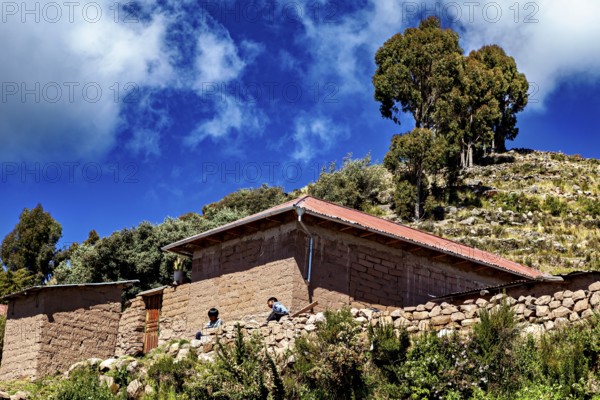 Rustic farm houses with two people and trees under a blue sky full of clouds, the countryside and farmhouses on the island of Taquile in Lake Titicaca in Peru