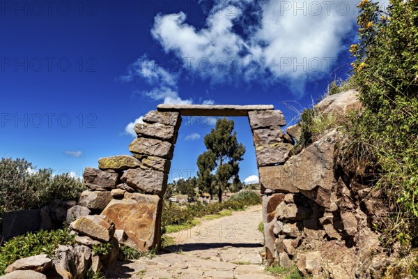 A rectangular stone arch under a cloudy sky, with a path that leads into nature, stone gates on Taquile Island in Lake Titicaca in Peru