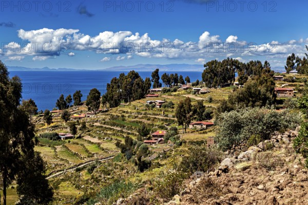 A terraced village stretches along a hill overlooking a blue lake, countryside and farmhouses on Taquile Island in Lake Titicaca in Peru