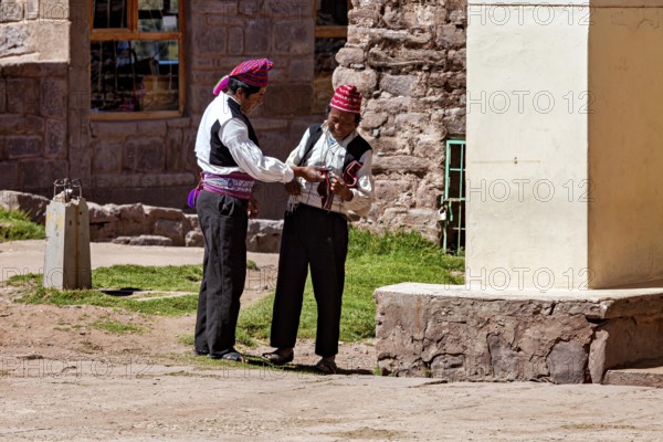 Two men in traditional dress talk next to a stone wall, The Knitting Men on Taquile Island in Lake Titicaca in Peru
