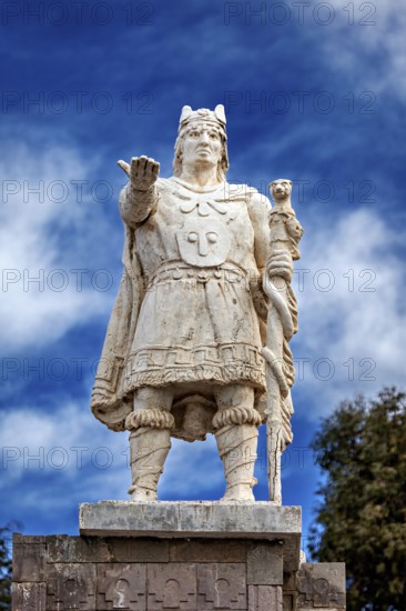 Stone statue of a warrior with a raised hand against a blue sky, Great Inca monument on Taquile Island in Lake Titicaca in Peru