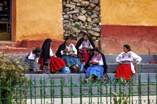 Group of woman in colorful traditional clothing sit on stairs and talk vividly, the woman on Taquile Island in Lake Titicaca in Peru
