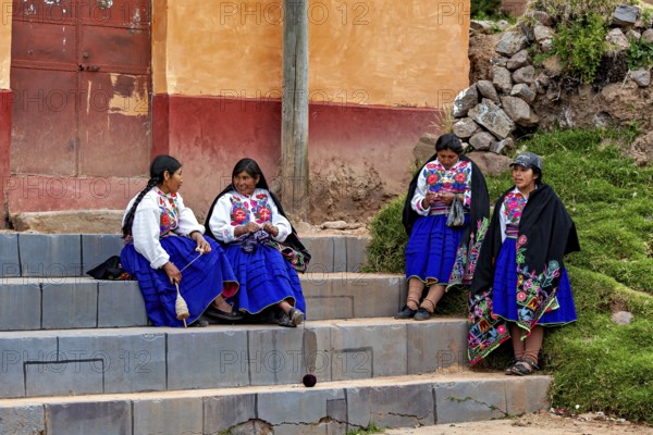 Group of woman in traditional dress sitting on stairs and talking, The woman on Taquile Island in Lake Titicaca in Peru