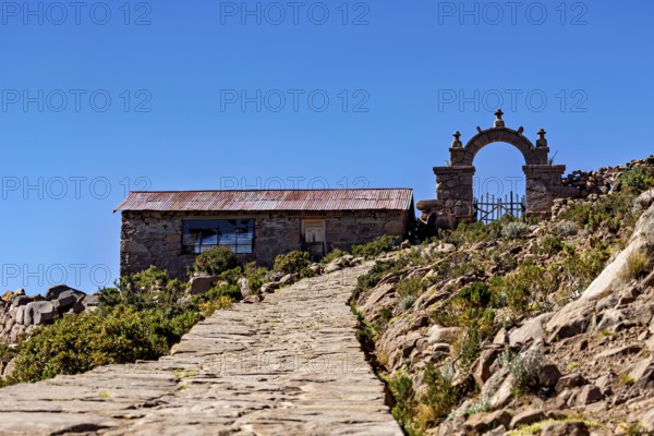 Stone house with archway along a path under a blue sky, stone gates on Taquile Island in Lake Titicaca in Peru