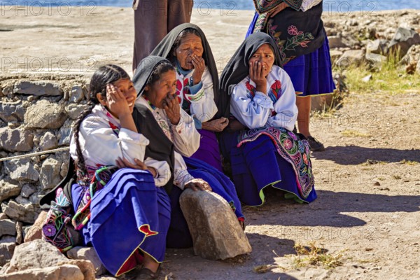 Elderly woman in traditional clothing sitting in the sun on a stone wall, the woman on Taquile Island in Lake Titicaca in Peru