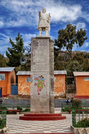 Stone figure and reliefs in front of colorful houses under blue sky, quiet environment, Great Inca monument on the island of Taquile in Lake Titicaca in Peru