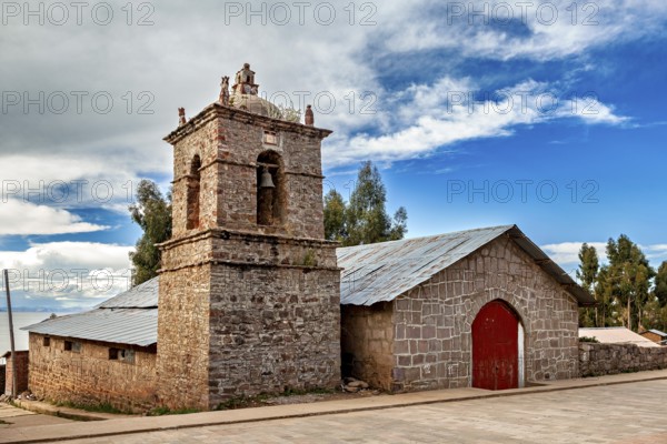Stone church building with red gate and bell tower under changing skies, The historic church on Taquile Island in Lake Titicaca in Peru