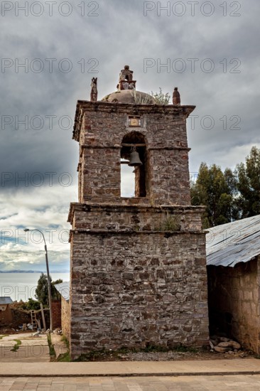 An old stone bell tower in cloudy sky surrounded by rustic landscape, The historic church on Taquile Island in Lake Titicaca in Peru