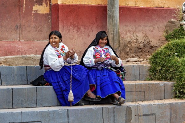 Two woman in traditional clothing sit on stairs and spin by hand, the woman on Taquile Island in Lake Titicaca in Peru