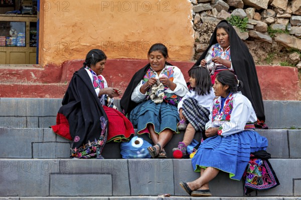Women and children in traditional clothing sit on steps and interact with each other, the woman on Taquile Island in Lake Titicaca in Peru