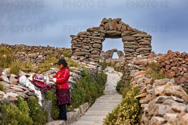 Woman next to clothes on traditional path with stone walls, stone gates on Taquile Island in Lake Titicaca in Peru