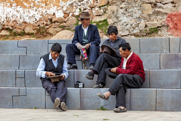 Four men in traditional clothing sit relaxed on stone steps in an urban setting, men sit together on the island of Taquile in Lake Titicaca in Peru