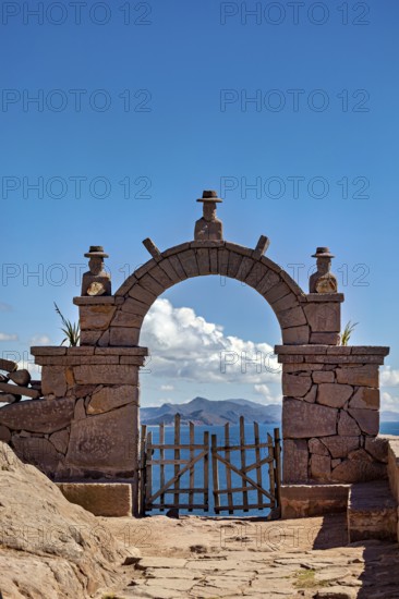 A stone archway with decorations that opens up to a vast mountain panorama under a blue sky, stone gates on the island of Taquile in Lake Titicaca in Peru