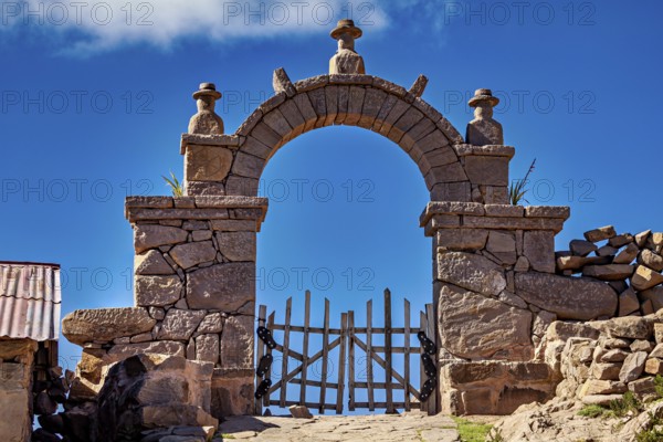 Massive stone archway with decorated sculptures rising into a clear blue sky, stone gates on Taquile Island in Lake Titicaca in Peru