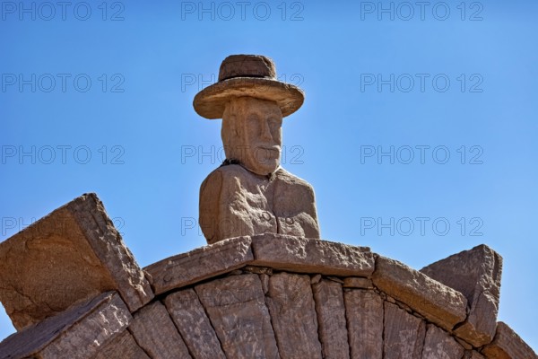 Stone bust with hat on an archway, artfully designed against a clear blue sky, stone gates on the island of Taquile in Lake Titicaca in Peru
