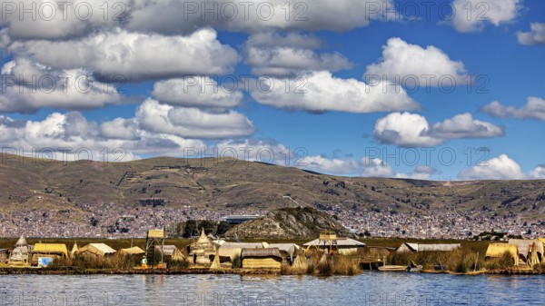 Village with traditional lakeside buildings surrounded by hills and clouds, The floating reed islands of Uros in Lake Titicaca in Peru