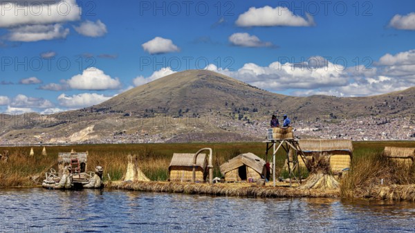Reed huts and lakeside observation tower with mountains in the background under blue sky, The floating reed islands of Uros in Lake Titicaca in Peru