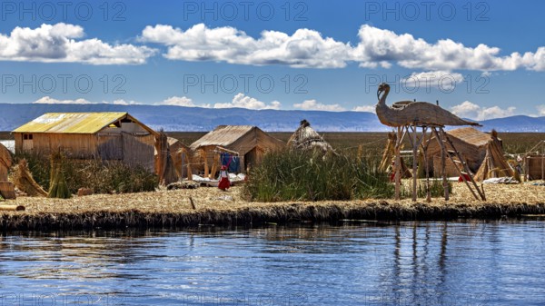 Handmade huts with thatched roofs and boats on the edge of a lake under a cloudy sky, The floating reed islands of the Uros in Lake Titicaca in Peru