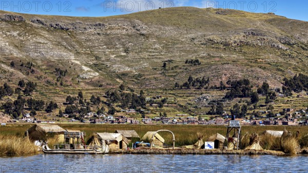 Small reed village on the shore with mountains in the background under a blue sky, The floating reed islands of Uros in Lake Titicaca in Peru
