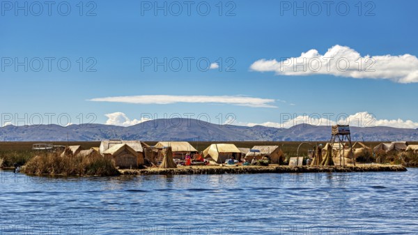 Reed huts on an island in the lake under a clear sky with mountains in the background, The floating reed islands of the Uros in Lake Titicaca in Peru