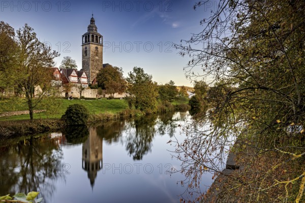 Church on the river, surrounded by autumnal trees with beautiful reflections in calm water, The town of Bad Sooden Allendorf an der Werra in the Werra Meissner district of Hesse