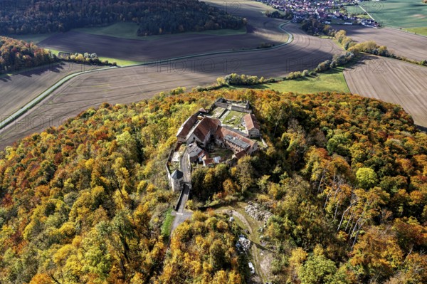 Aerial view of a castle on a hill surrounded by autumnal forest with colorful trees, Gleichenstein Castle in the Eichsfeld district of Thuringia